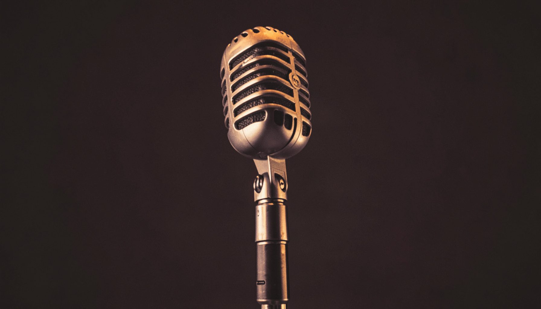 Warm duotone photograph of a vintage microphone on a stand, lit by soft amber and plum tones against a dark studio background.